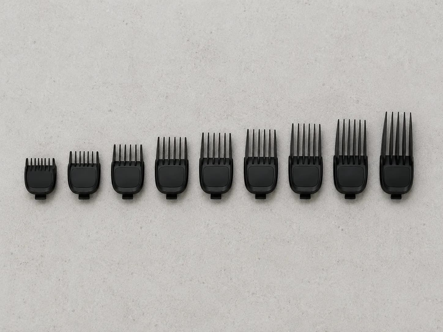 Black beard trimmer guard combs arranged from shortest to tallest on a light gray background, showing the gradual increase in cutting length for different trimming settings.