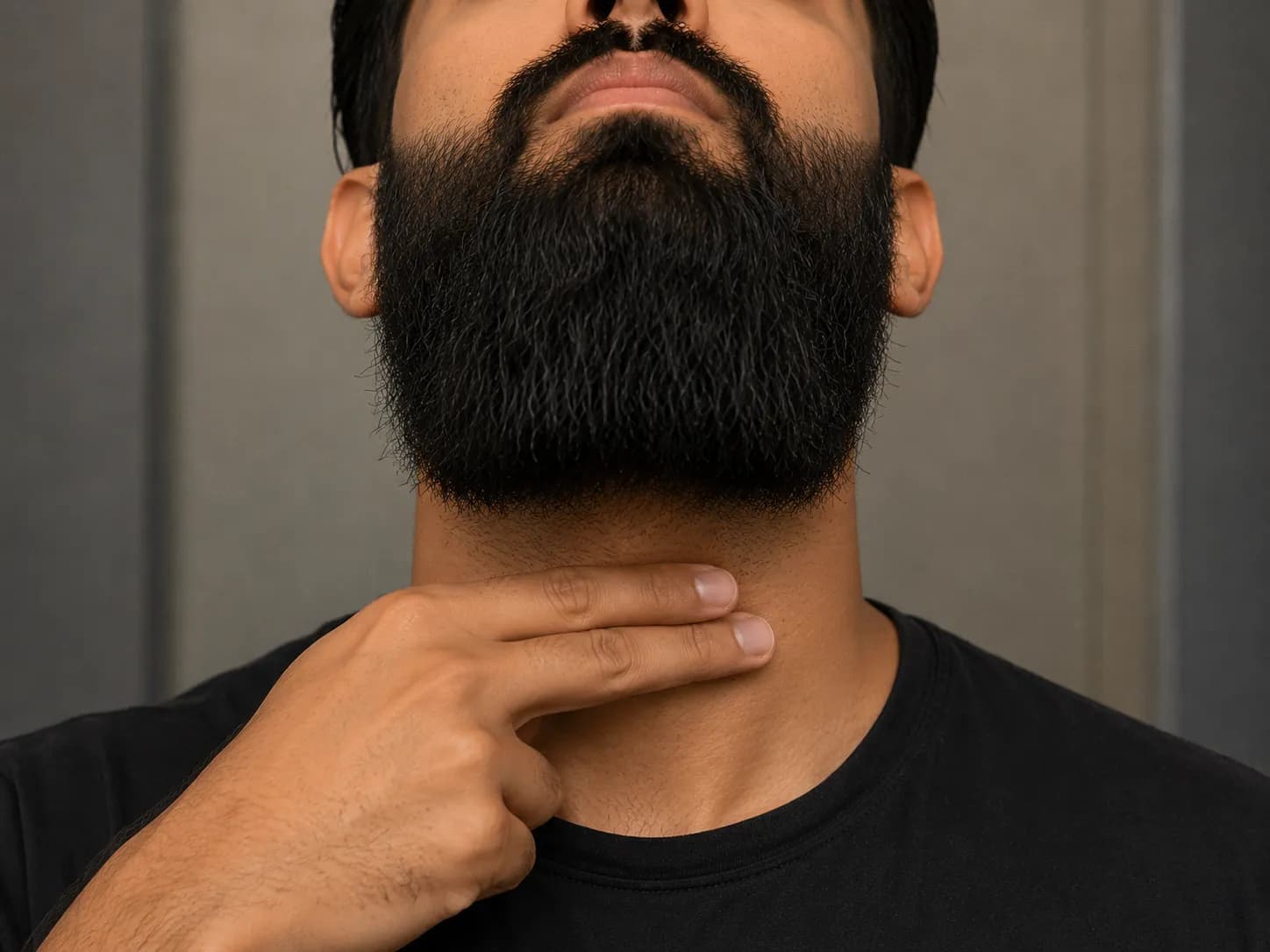 Man placing two fingers above the Adam's apple with his chin tilted up to mark the correct neckline position for trimming and maintaining a long beard.